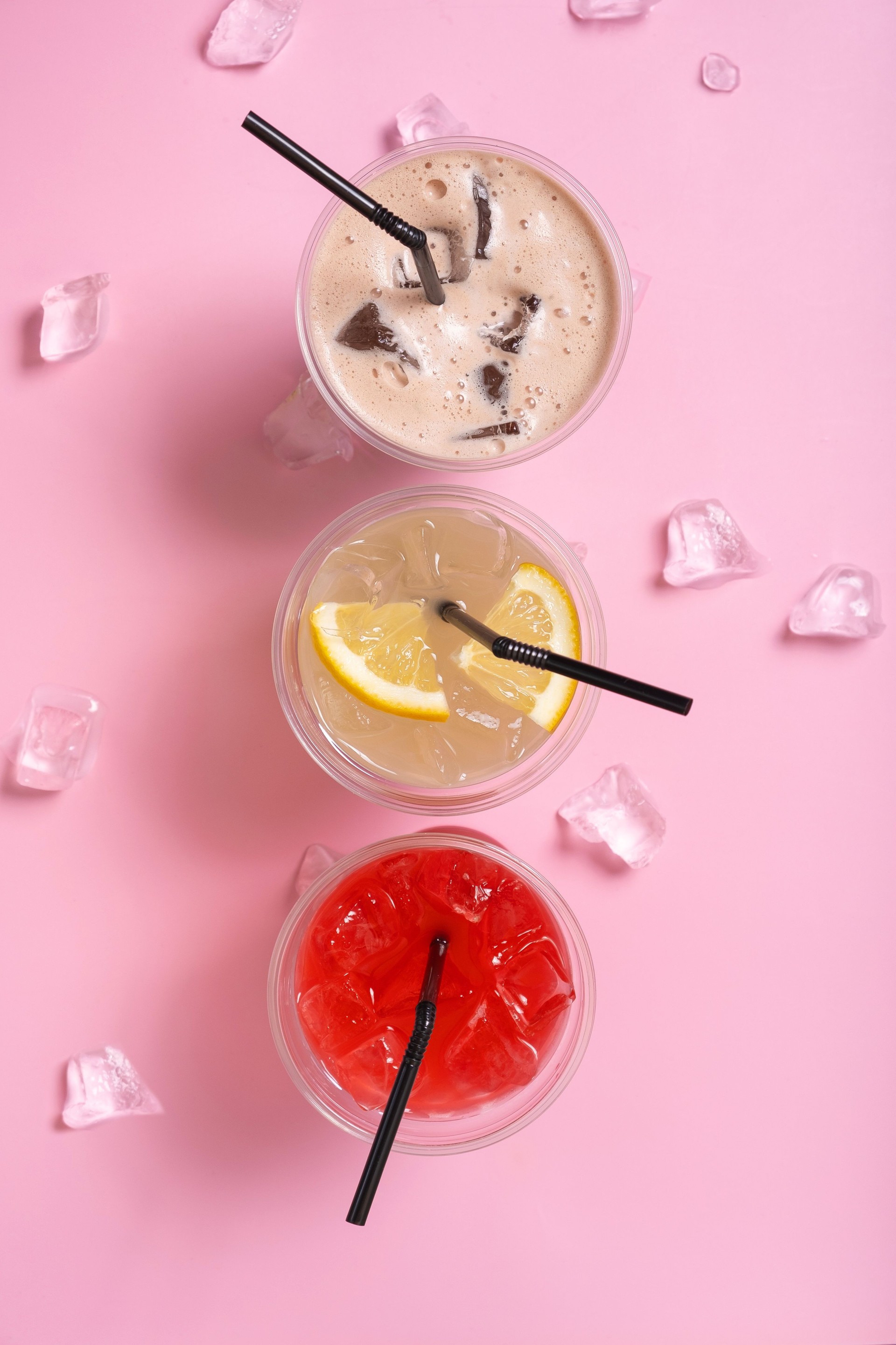 Colourful three takeaway glasses of summer drinks with ice top view on pink background